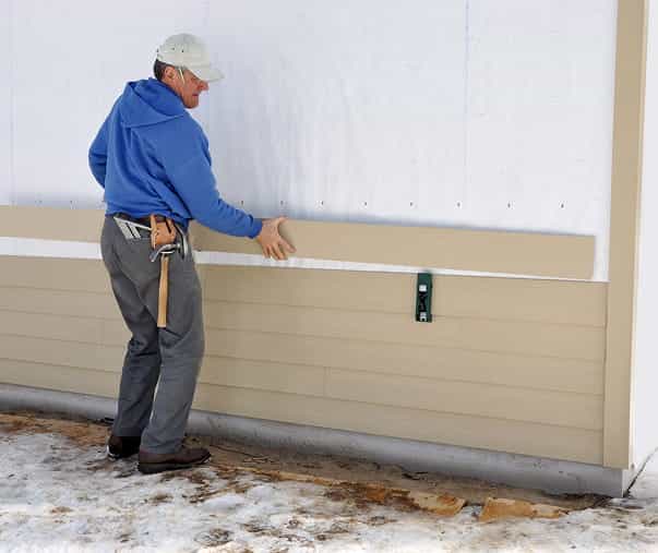 technicin attaching siding to house